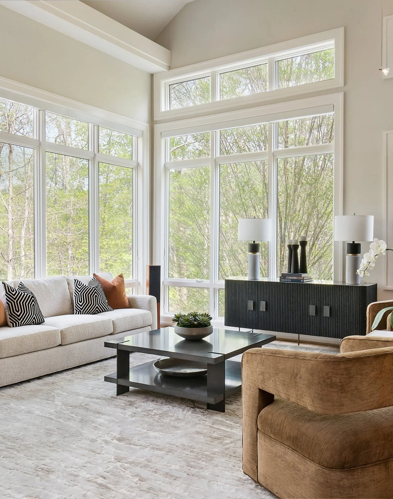 Vaulted living room with floor-to-ceiling windows onto woodland, cream sofa and a black fluted credenza